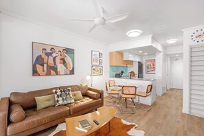 A modern living room with a brown leather sofa, a coffee table, and a cowhide rug. There is a dining area with a small kitchen in the background. - Funky Teneriffe - 2bed-2bath-balcony-1car (Brisbane)