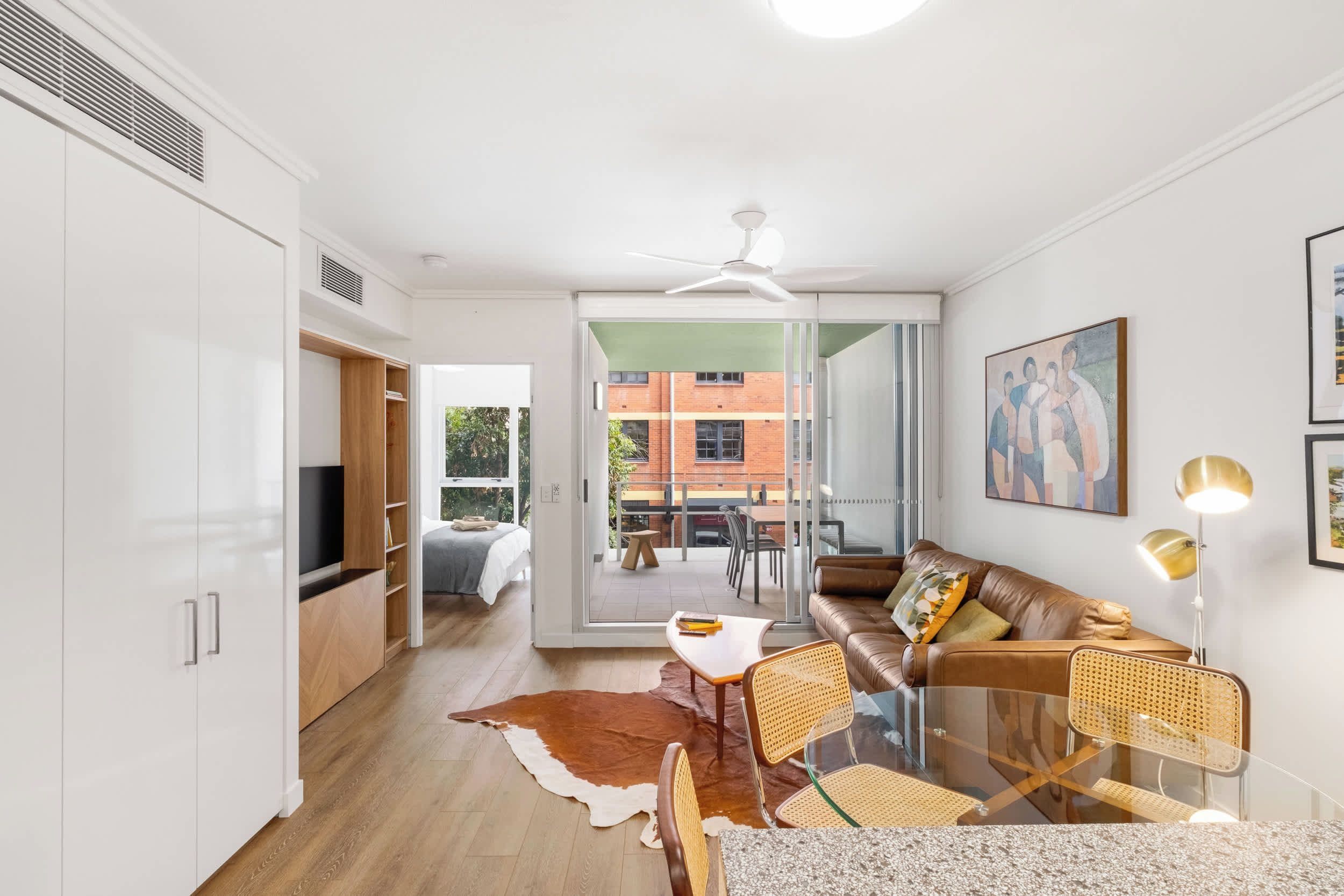 A modern apartment with a dining area, a sofa, a glass table, and a ceiling fan.