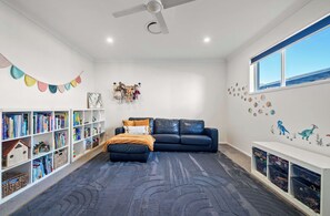 A child-friendly room with a bookshelf, a sofa, and a play area. - Sunset Cove - Bribie Island Waterfront Retreat (Bribie Island Region)
