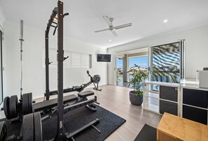 A modern home gym with a stationary bike, weight bench, and a ceiling fan. - Sunset Cove - Bribie Island Waterfront Retreat (Bribie Island Region)