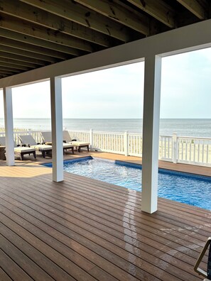 Eine Holzterrasse mit Pool, Liegestühlen und Blick auf den Ozean.