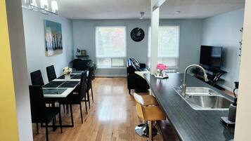 A modern kitchen with a bar area, dining space, and a living area with a sofa and TV.