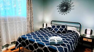 A bedroom with a bed, a nightstand, a wall decoration, and a window with curtains.