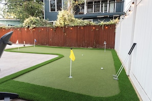 A miniature golf course with a green artificial turf, a yellow flag, and a wooden fence. - Luxe 4BR/3BA • Heated Pool + Gym, 5 Min Downtown (Austin)