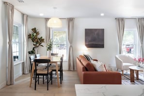 A modern living room with a dining area, a sofa, a coffee table, and a painting on the wall. - Luxe 4BR/3BA • Heated Pool + Gym, 5 Min Downtown (Austin)