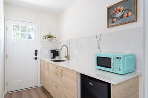 A modern kitchen with a white door, a sink, a coffee machine, a microwave, and a cabinet. - Luxe 4BR/3BA • Heated Pool + Gym, 5 Min Downtown (Austin)