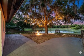 A tree with lights, a fire pit, and a pond in a landscaped outdoor area. - Lakefront 3BR Monthly Snowbird Rental, Private Pool, near The Villages (Fruitland Park)