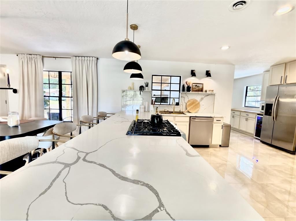 A modern kitchen with a large island, stainless steel appliances, pendant lighting, and a view of the outdoors.
