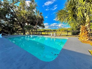 A swimming pool with a wooden deck, surrounded by trees and a clear sky. - Lakefront 3BR Monthly Snowbird Rental, Private Pool, near The Villages (Fruitland Park)
