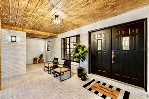 A reception area with a wooden ceiling, white brick walls, a black door, and a welcome mat. - Lakefront 3BR Monthly Snowbird Rental, Private Pool, near The Villages (Fruitland Park)