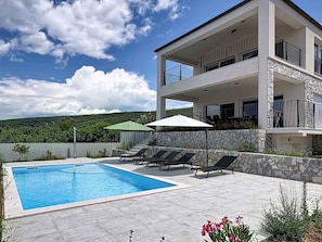 A modern two-story building with a swimming pool, outdoor seating, and a view of a green landscape. - Holiday home with swimming pool (Punat)