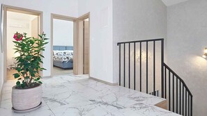 A hallway with a potted plant, a staircase with a black railing, and a bedroom with a bed and a window. - Holiday home with swimming pool (Punat)