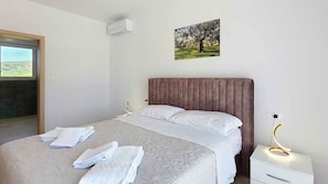 A bedroom with a bed, a bedside table with a lamp, a window, and a wall-mounted air conditioner. - Holiday home with swimming pool (Punat)