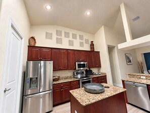 A modern kitchen with stainless steel appliances, wooden cabinets, and a granite countertop. - Perfect 4-bedroom house with AC in charming Cape Coral (Cape Coral)