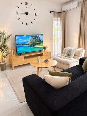 Ein modernes Wohnzimmer mit Flachbildfernseher, einer Couch, einem Couchtisch und einer Wanduhr.