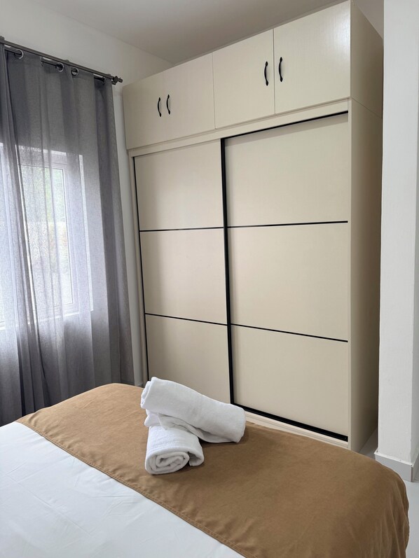 Ein Schlafzimmer mit einem Bett, einem großen Kleiderschrank und einem Fenster mit Vorhängen.