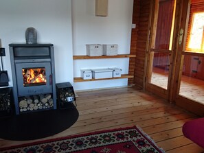 A cozy room with a wood-burning stove, shelves with storage boxes, and a wooden floor. - Haus am See by Interhome (Frymburk)