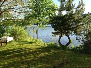 Un cadre idyllique au bord d’un lac, avec une table et des chaises, entouré d’arbres et d’une pelouse.