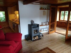 L’intérieur chaleureux d’un chalet avec un poêle à bois, un canapé rouge et un coin cuisine.