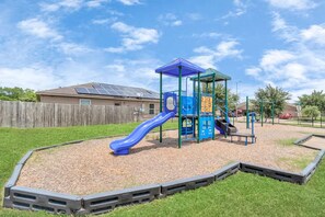 Ein Spielplatz mit einer blauen Rutsche und Klettergerüsten, umgeben von einem Holenzaun und einer Rasenfläche.