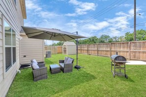 Un giardino sul retro con patio, barbecue e zona salotto coperta.