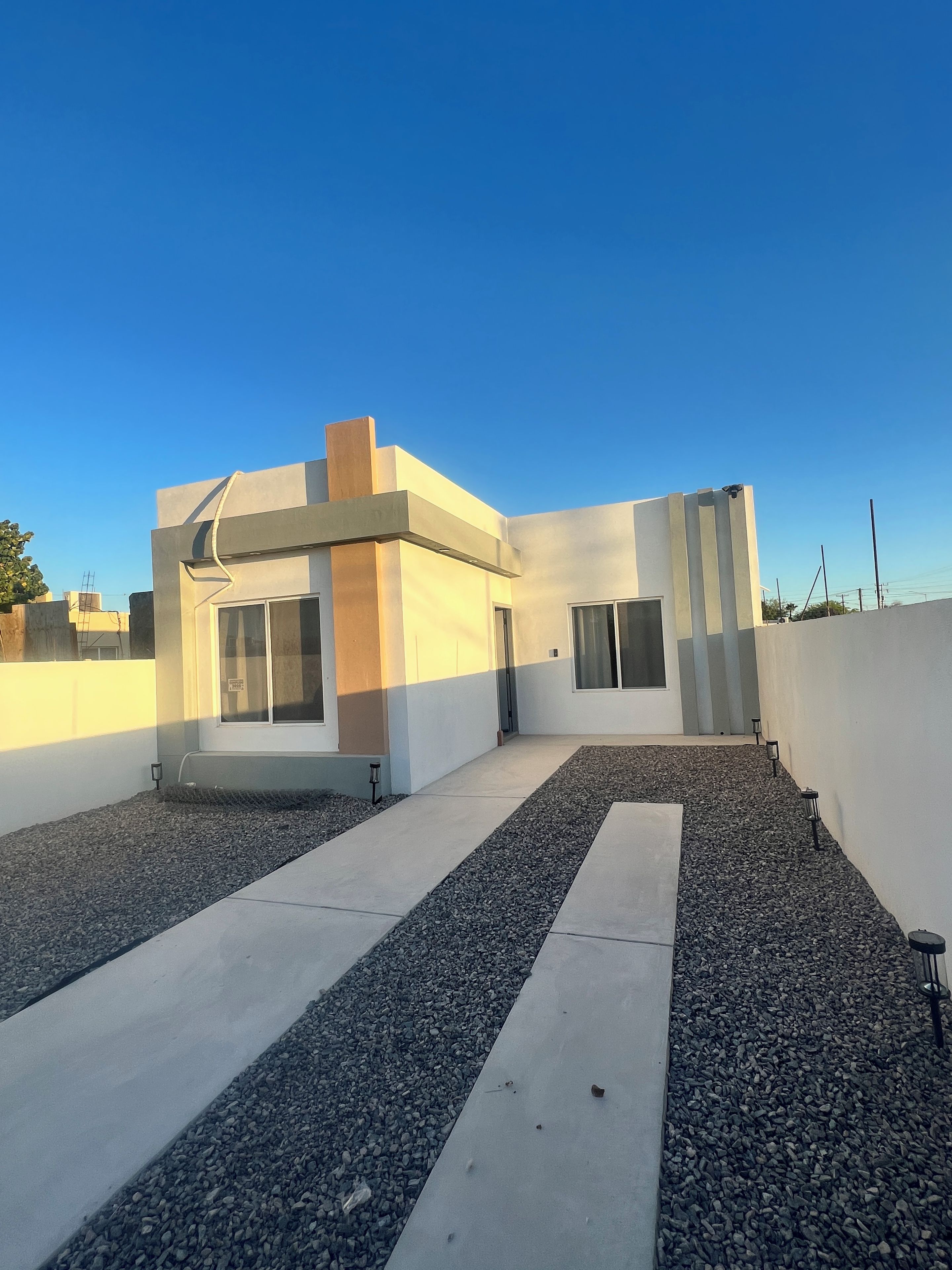 A modern building with a flat roof, a small entrance, and a gravel pathway leading to the entrance.