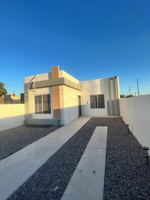 A modern building with a flat roof, a small entrance, and a gravel pathway leading to the entrance.