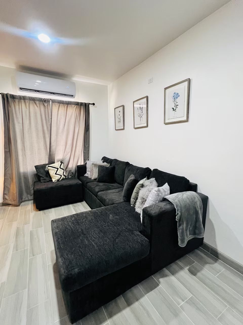 A modern living room with a sectional sofa, a small ottoman, and a wall-mounted air conditioner.