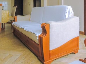 A wooden sofa with a white cover in a room with a tiled floor.