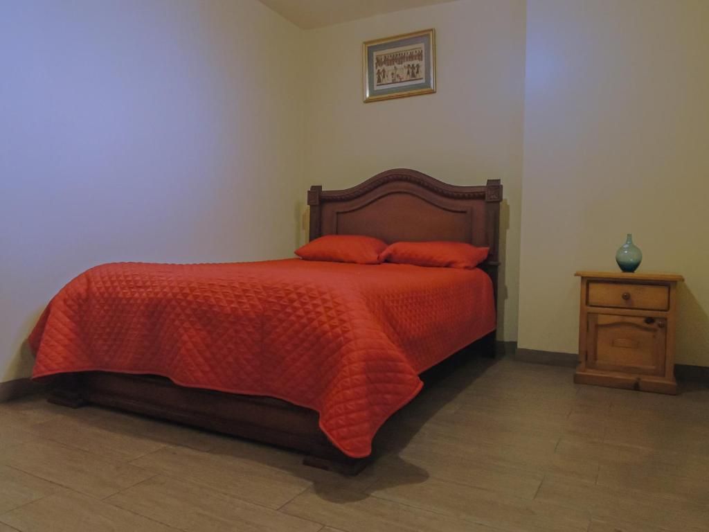 Una cama individual con cabecera de madera y manta roja en una habitación con mesita de noche de madera y un florero.