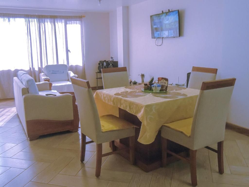 Een eetgedeelte met een tafel voor vier personen, omringd door stoelen, in een kamer met een bank en een televisie aan de muur.