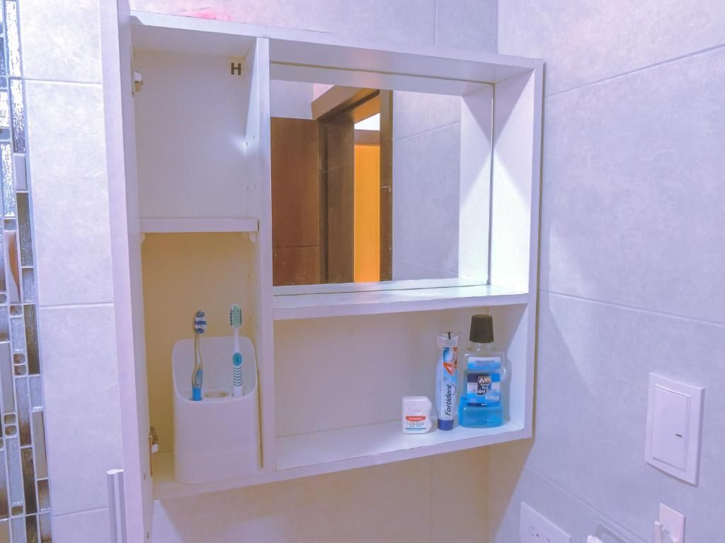 Une salle de bain avec un meuble-lavabo blanc, un miroir et une étagère où sont posées des brosses à dents et du dentifrice.