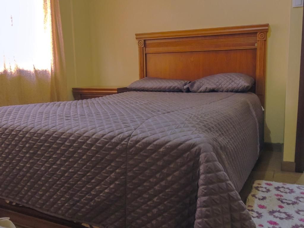 Een bed met een gewatteerde spreidek, een houten hoofdbord en een nachtkastje met een lamp.