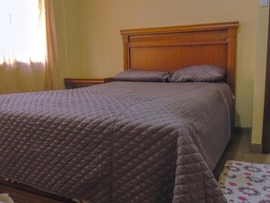 Cama com cobertura acolchoada, cabeceira de madeira e mesa de cabeceira com luminária.