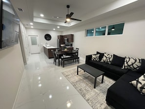 A modern living room with a black sofa, a coffee table, and a dining area with a table and chairs. - Apartment in Weslaco, TX. 3BR / 2 BA (Weslaco)