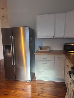 A kitchen with a stainless steel refrigerator, white cabinets, a microwave, and wooden flooring. - Comfortable, Pet Friendly, Historic Home in Huntsville (Huntsville)