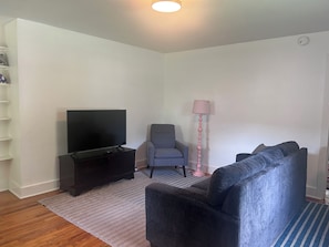 A living room with a flat-screen TV, a grey armchair, a sofa, a pink floor lamp, and a striped rug. - Comfortable, Pet Friendly, Historic Home in Huntsville (Huntsville)