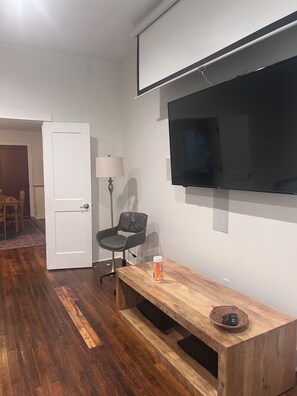A room with a wooden bench, a television mounted on the wall, a door, and a lamp. - Comfortable, Pet Friendly, Historic Home in Huntsville (Huntsville)