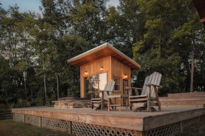 Een houten hut met een terras, twee Adirondack-stoelen en een stenen open haard.