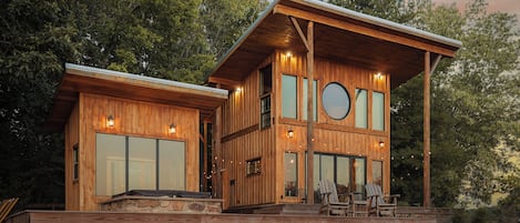 A wooden cabin with a deck, large windows, and a circular skylight.
