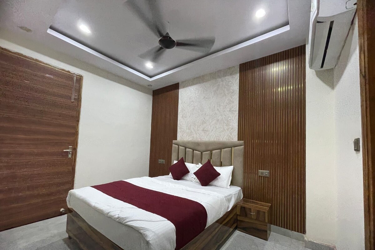 A hotel room with a bed, a ceiling fan, an air conditioning unit, and wooden paneling on the walls.