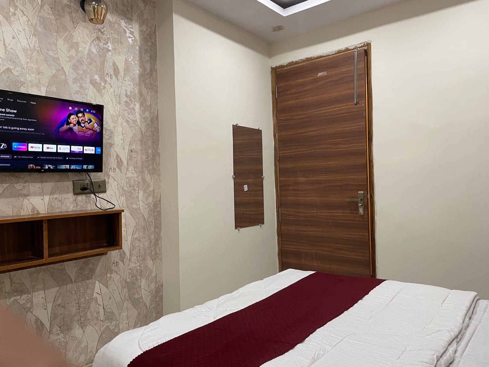 A bedroom with a bed, a television mounted on the wall, and a wooden wardrobe.