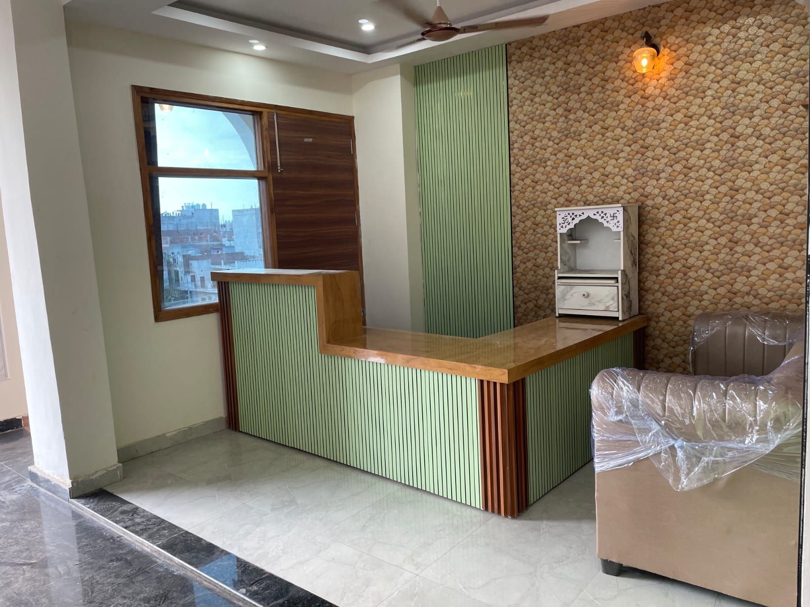 A reception area with a wooden counter, a green vertical panel, a white decorative cabinet, and a plastic-covered chair.