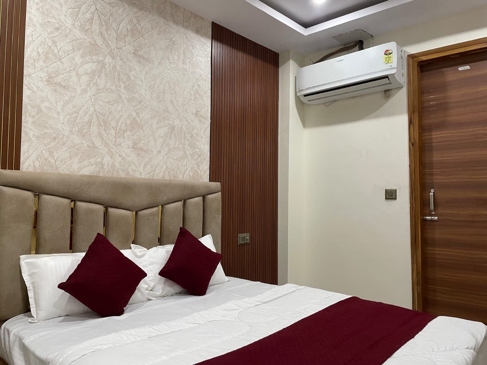 A hotel room with a bed, a wall-mounted air conditioner, and a wooden door.