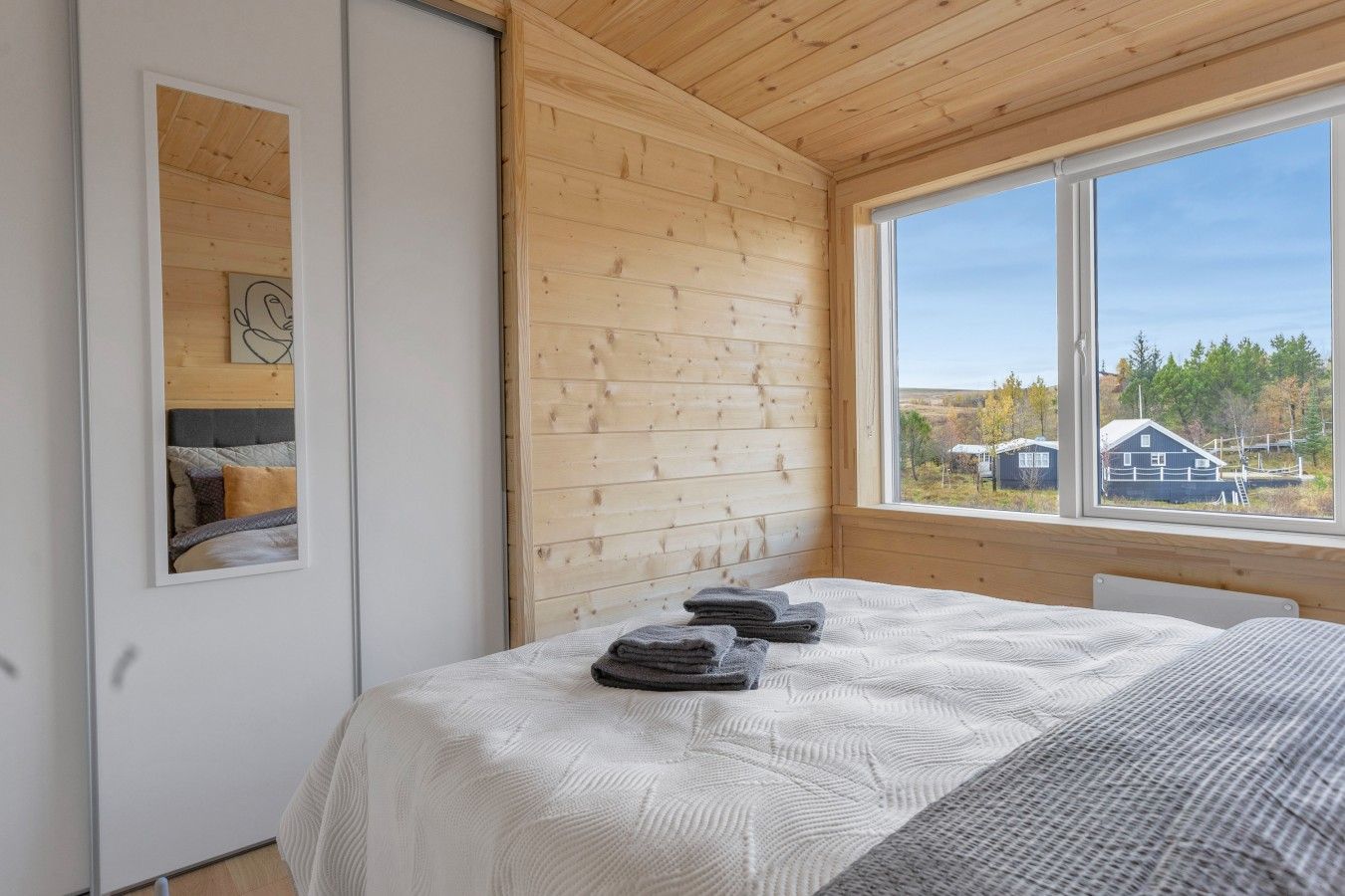 Une pièce avec un lit, une fenêtre donnant sur des maisons et un plafond en bois.