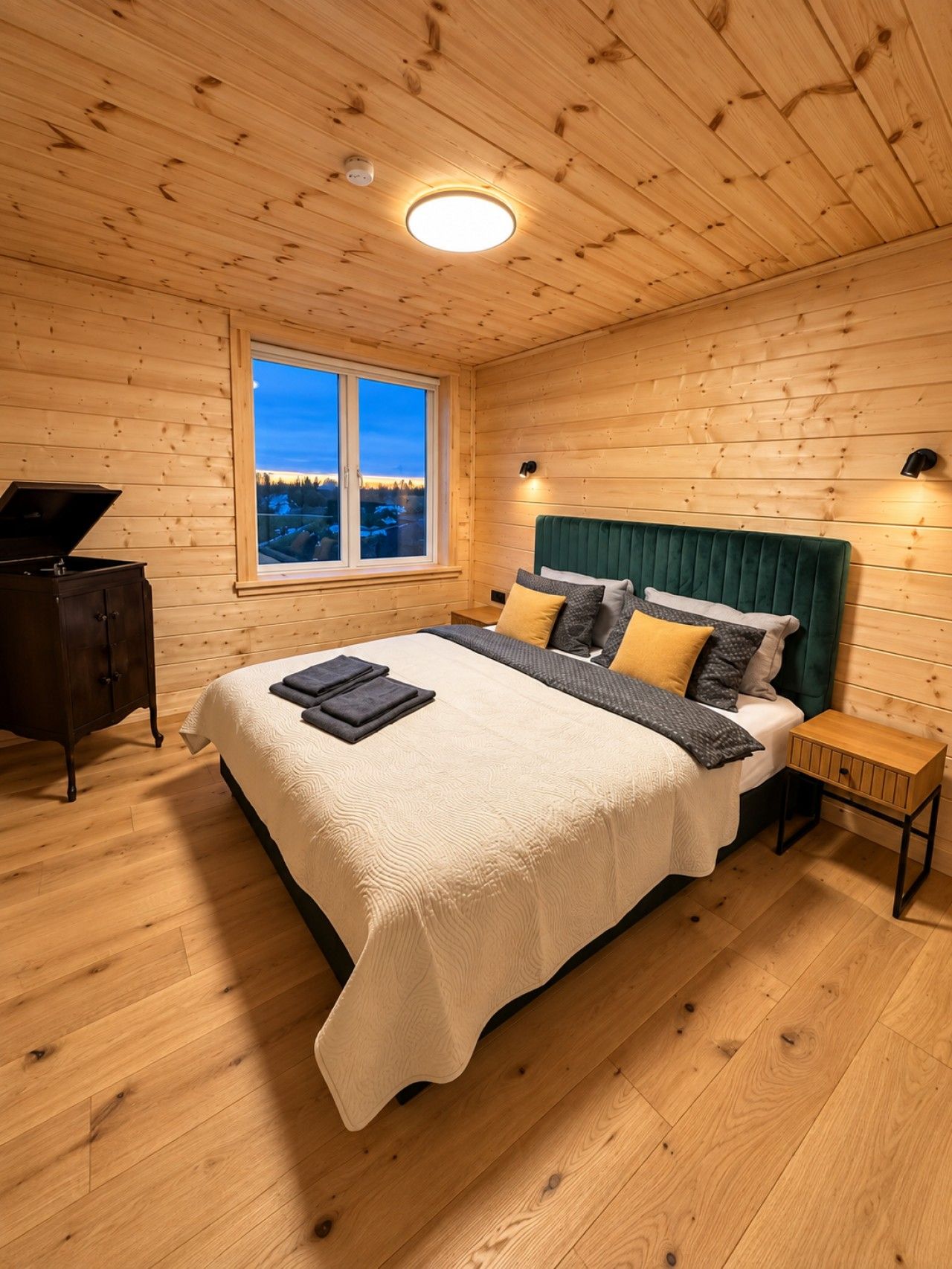 Une chambre à coucher aux murs lambrissés, comprenant un lit, des tables de chevet, une commode et une fenêtre donnant sur un paysage agréable.