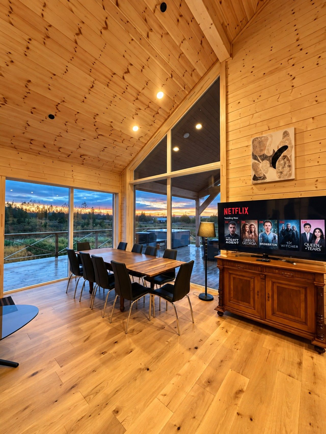 Une pièce spacieuse avec un plafond en bois, de grandes fenêtres, une table à manger en bois avec des chaises et un téléviseur diffusant des programmes Netflix.