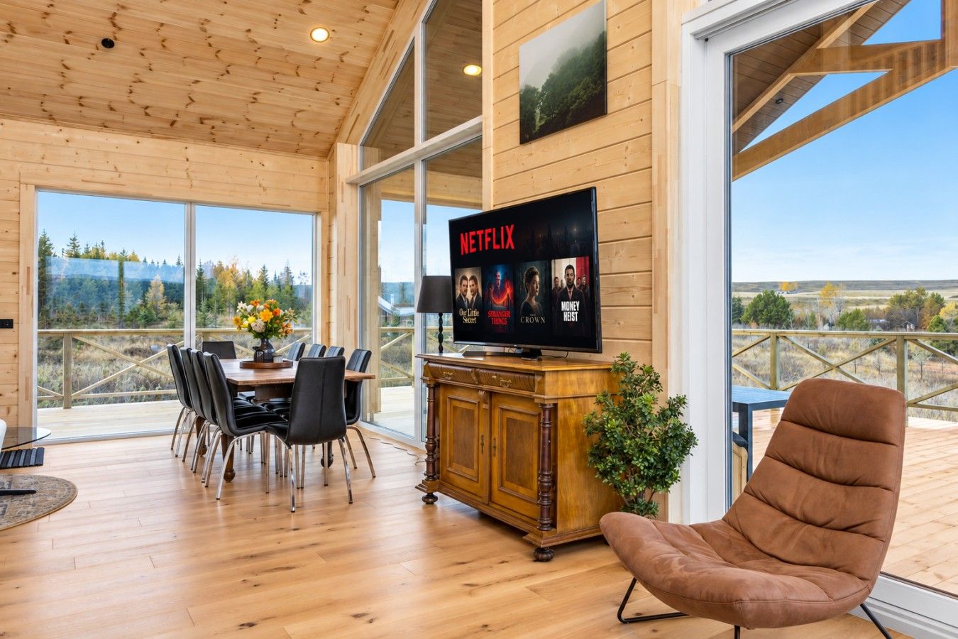 A wooden interior with a dining area, a television displaying Netflix, and a view of the outdoors.