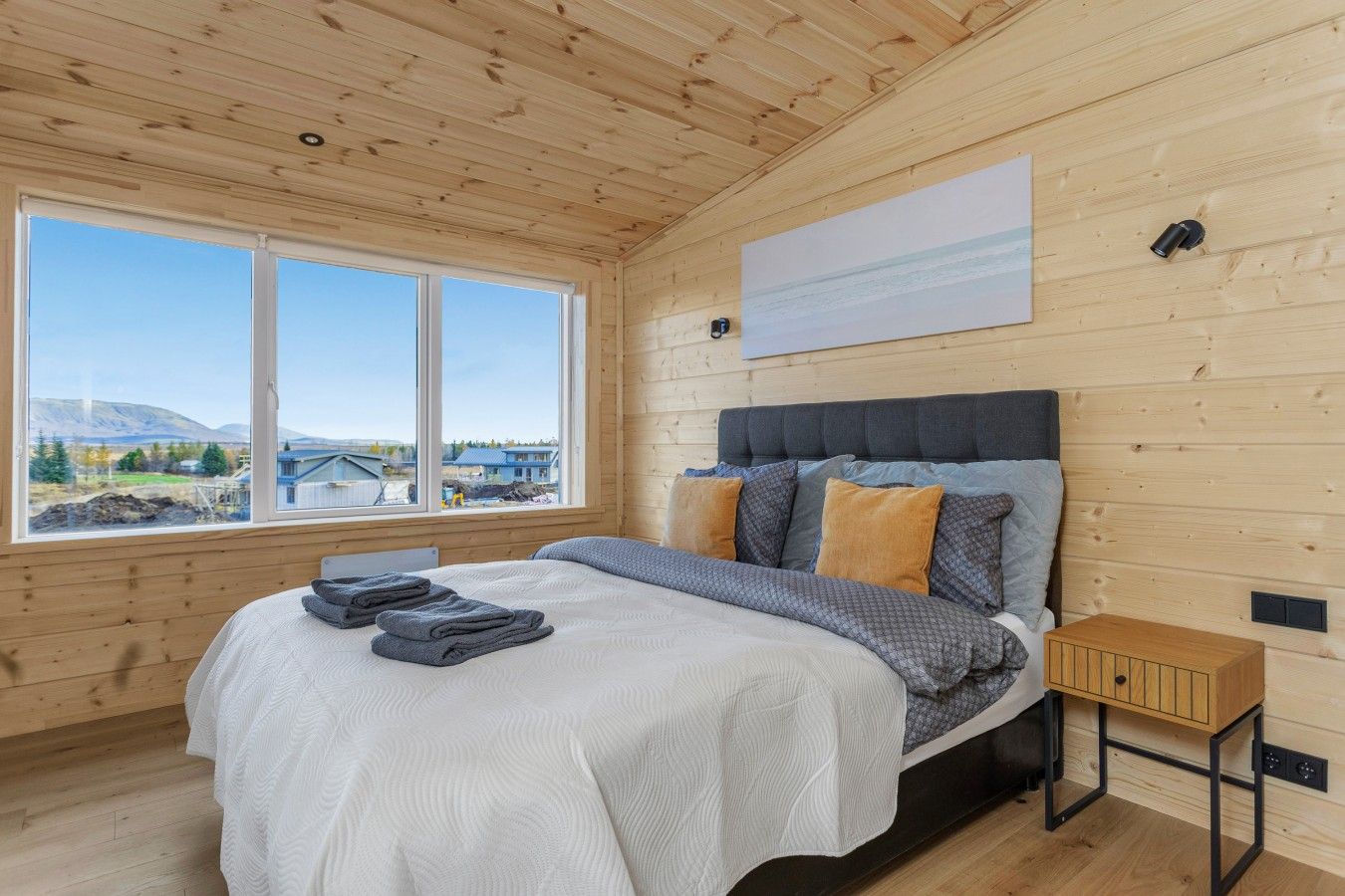 A bedroom with a bed, a nightstand, and a window with a view of a bridge and mountains.