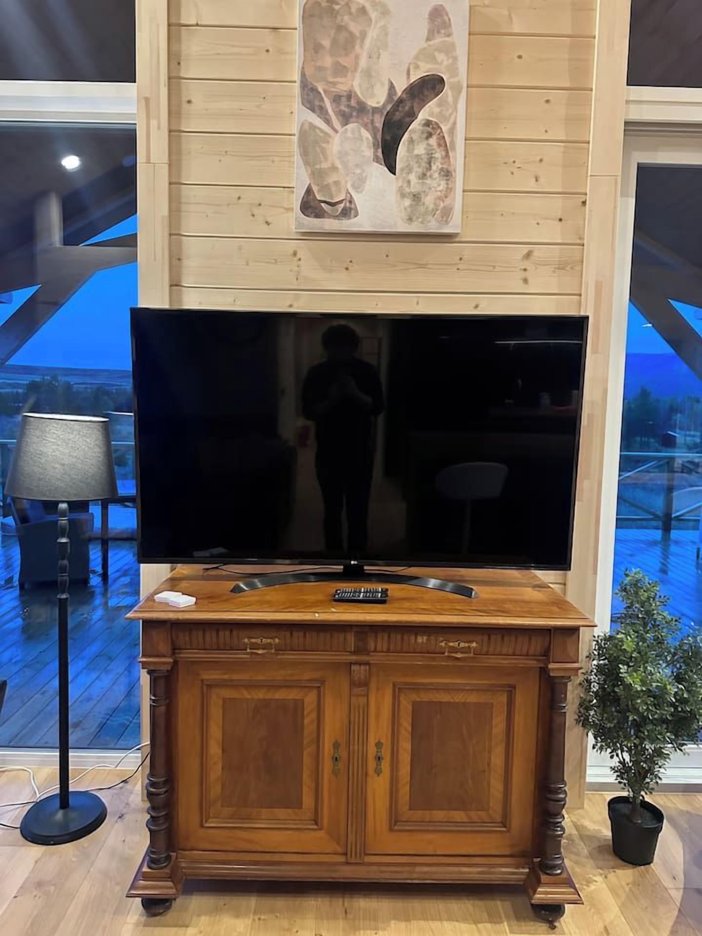 Een houten kast met een flatscreen televisie, een schilderij erboven en een plant in een pot ernaast.
